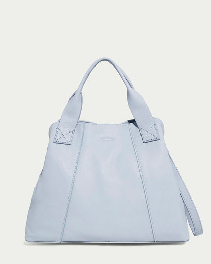 The Ada Triple Entry Satchel by American Leather Co. is a light blue leather handbag with two short handles, an adjustable crossbody strap, and a small embossed logo. Its elegant design features subtle stitching details on genuine American leather against a neutral background.