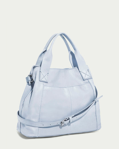 The Ada Triple Entry Satchel by American Leather Co. is a light blue, structured satchel made from genuine American leather. It features short handles, a detachable adjustable crossbody strap, visible stitching, and a buckle detail on its rounded shape against a plain background.