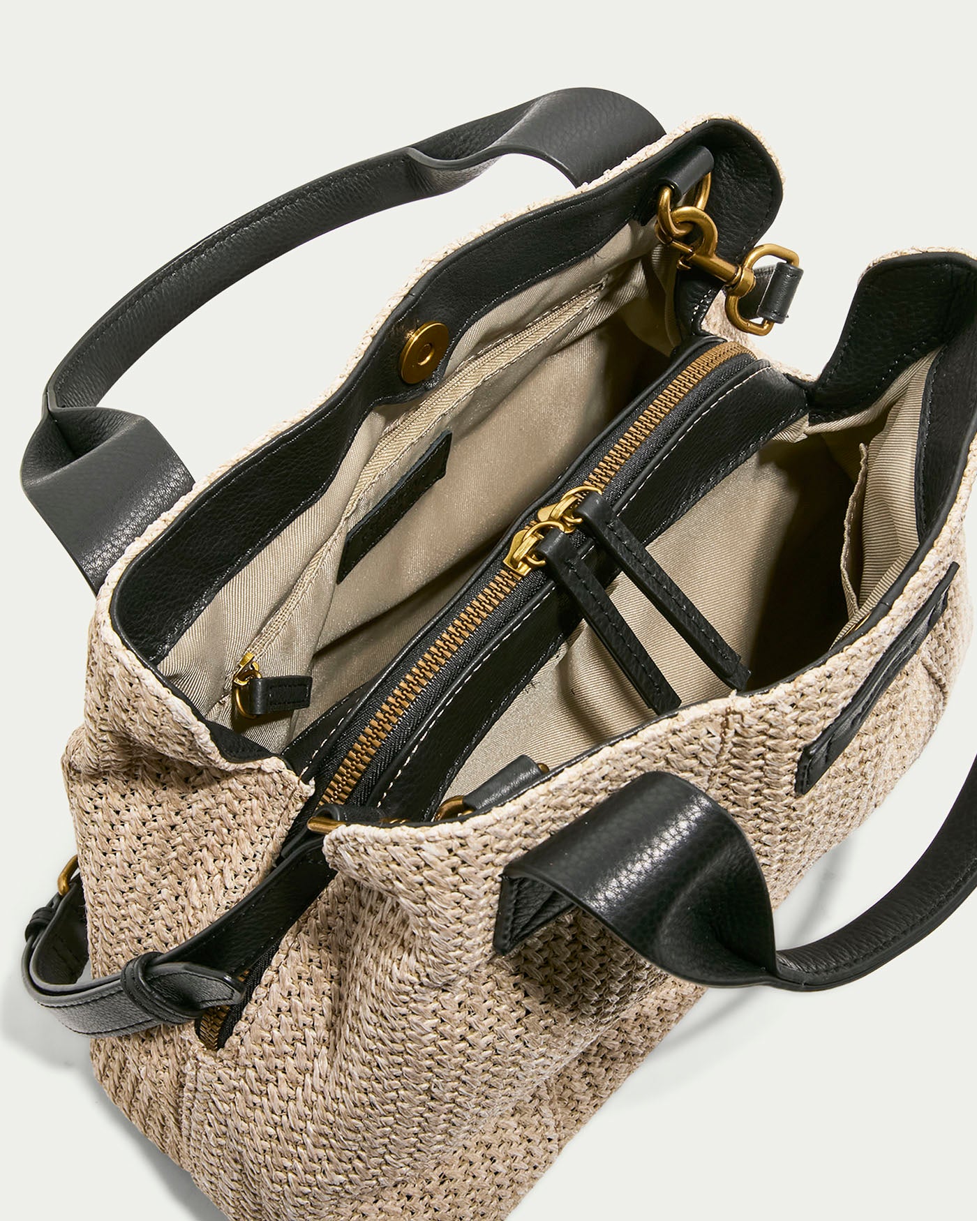 The Ada Triple Entry Satchel Raffia with Black by American Leather Co. features an open tan woven design, black leather handles and trim, and a beige interior with gold hardware. It offers multiple compartments including a zippered pocket, providing a versatile structured satchel feel.