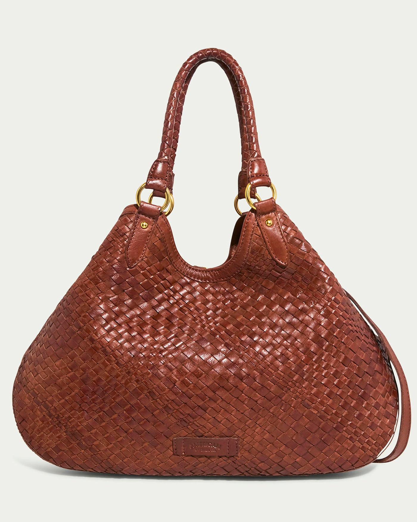 The Blair Convertible Tote from American Leather Co. is a spacious brandy genuine woven leather handbag with dual braided handles and gold hardware, boasting intricate detailing and a smooth, polished look, ideal for any occasion.