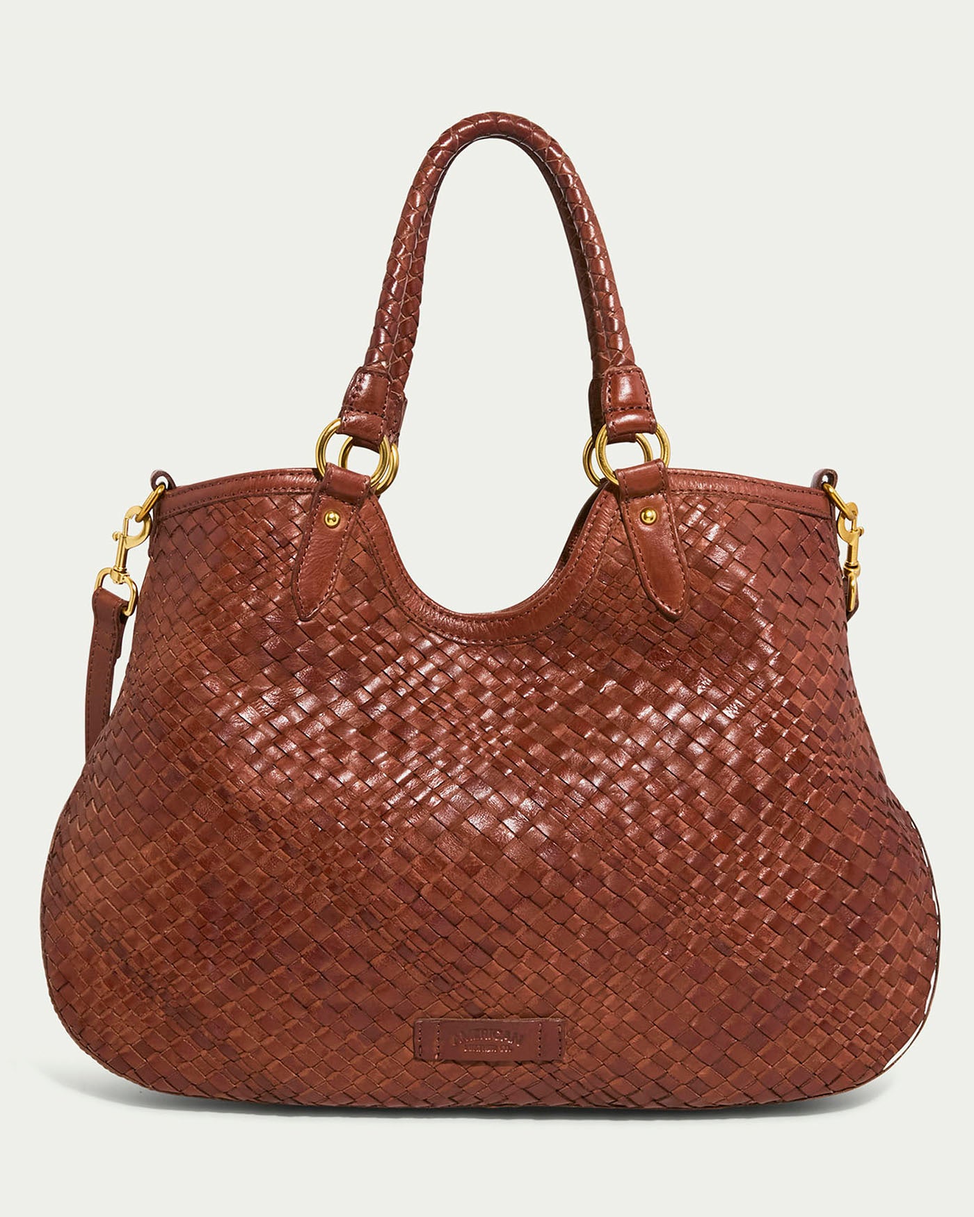 The Blair Convertible Tote by American Leather Co. is a large brown bag made from genuine woven leather, highlighted with gold hardware and two handles. Its detailed texture offers a rich and stylish look, making it perfect for any occasion.