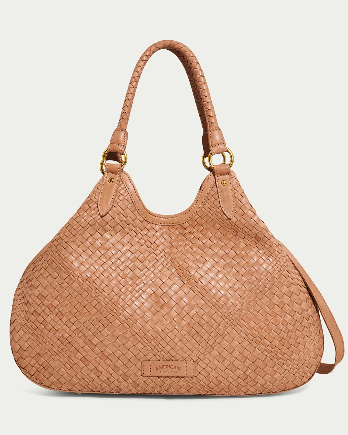 The Blair Convertible Tote by American Leather Co. in nutmeg features genuine woven leather with two braided handles and gold-tone metal rings. This slouchy design includes a small logo tag at the bottom, balancing elegance with everyday practicality.