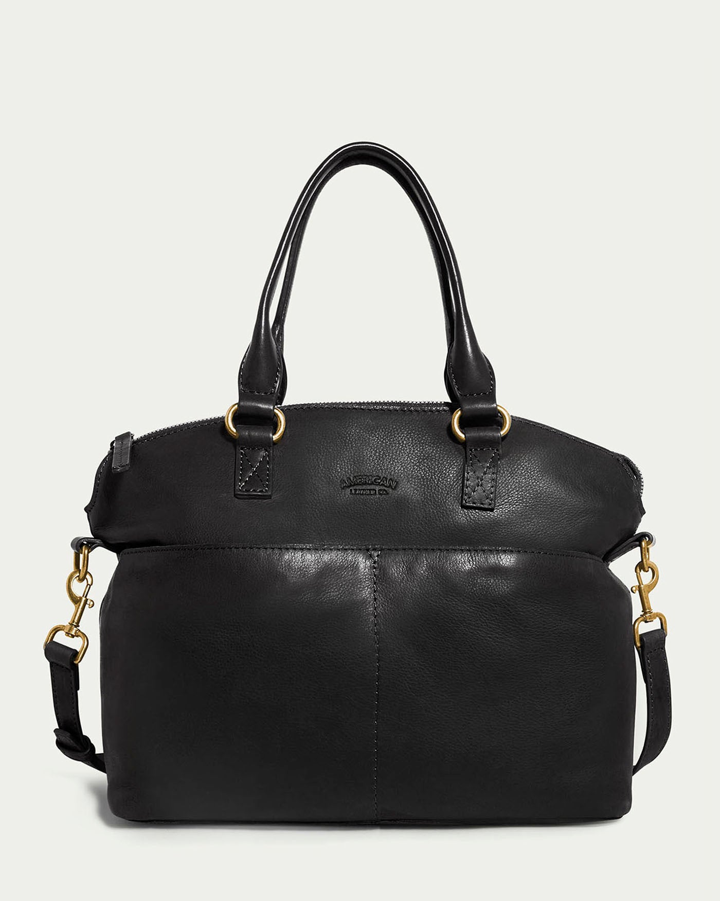 The Carrie Dome Satchel by American Leather Co. is a black leather handbag with dual handles, a detachable crossbody strap, gold-tone hardware, and features a curved zippered top and subtle front stitched detailing.