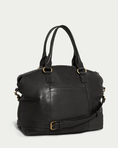 The Carrie Dome Satchel by American Leather Co. is a stylish black leather bag with dual handles and an adjustable crossbody strap. It features gold-tone hardware, two buckles, visible seam stitching, and offers a soft, structured shape made from genuine leather.