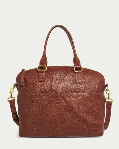 The Carrie Dome Satchel by American Leather Co. is a premium brown leather bag with embossed floral patterns. It includes two short handles, a detachable adjustable crossbody strap with gold hardware, and a zip closure on top for security.