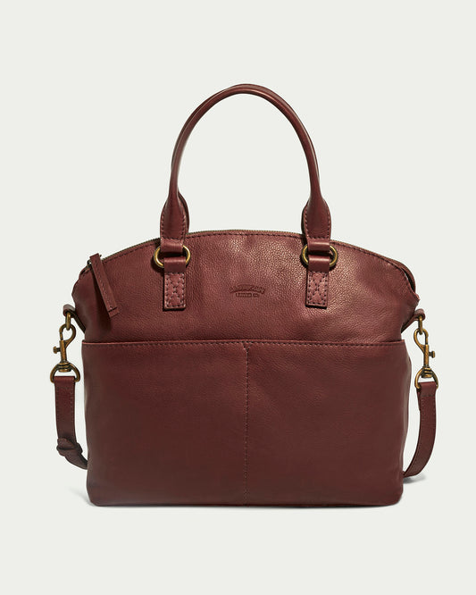 The Carrie Dome Satchel by American Leather Co. is a burgundy leather bag with antique brass hardware, top handles, and an adjustable crossbody strap. Made from genuine American leather, it features a front pocket and an embossed logo on the front.