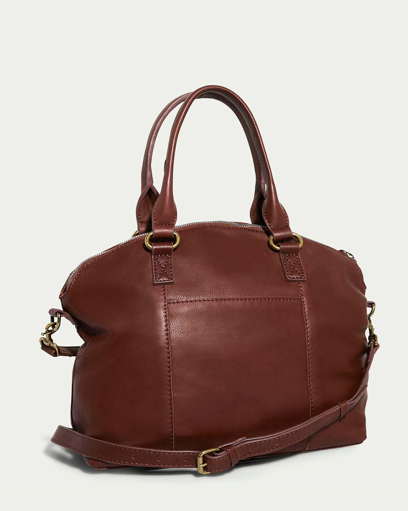 The Carrie Dome Satchel by American Leather Co. is a brown leather bag with dual handles and an adjustable crossbody strap. It features gold-tone hardware, a smooth texture, and a simple, elegant design against a light background.