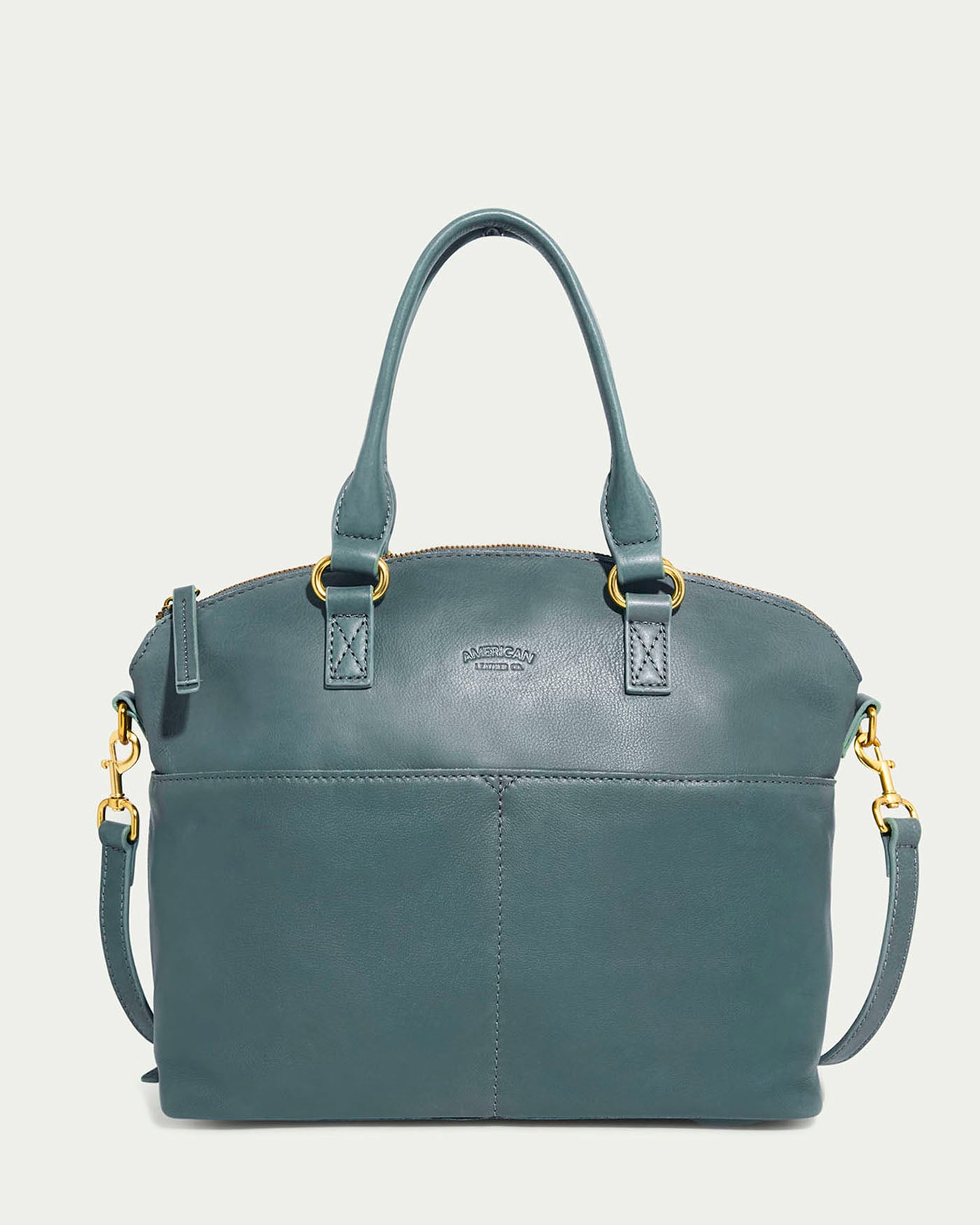 The Carrie Dome Satchel by American Leather Co. in Sage Leaf is crafted from genuine American leather. It features dual handles, an adjustable crossbody strap, gold-tone hardware, a zip closure, and a subtle logo embossing near the top.