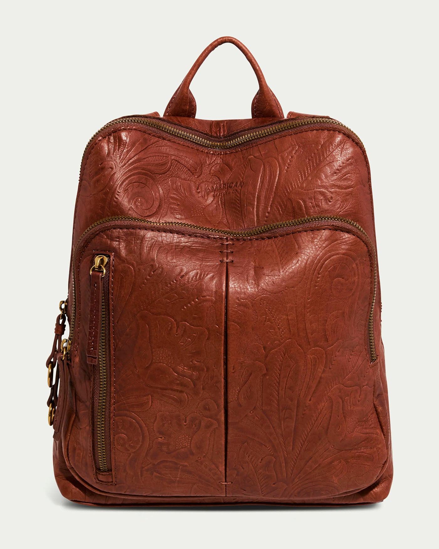 The Cleveland Backpack by American Leather Co. in Brandy Tooled features a floral embossed design with antiqued hardware. It has two front zippered pockets, a top handle, and elegant gold zippers, combining style and functionality with genuine American leather craftsmanship.