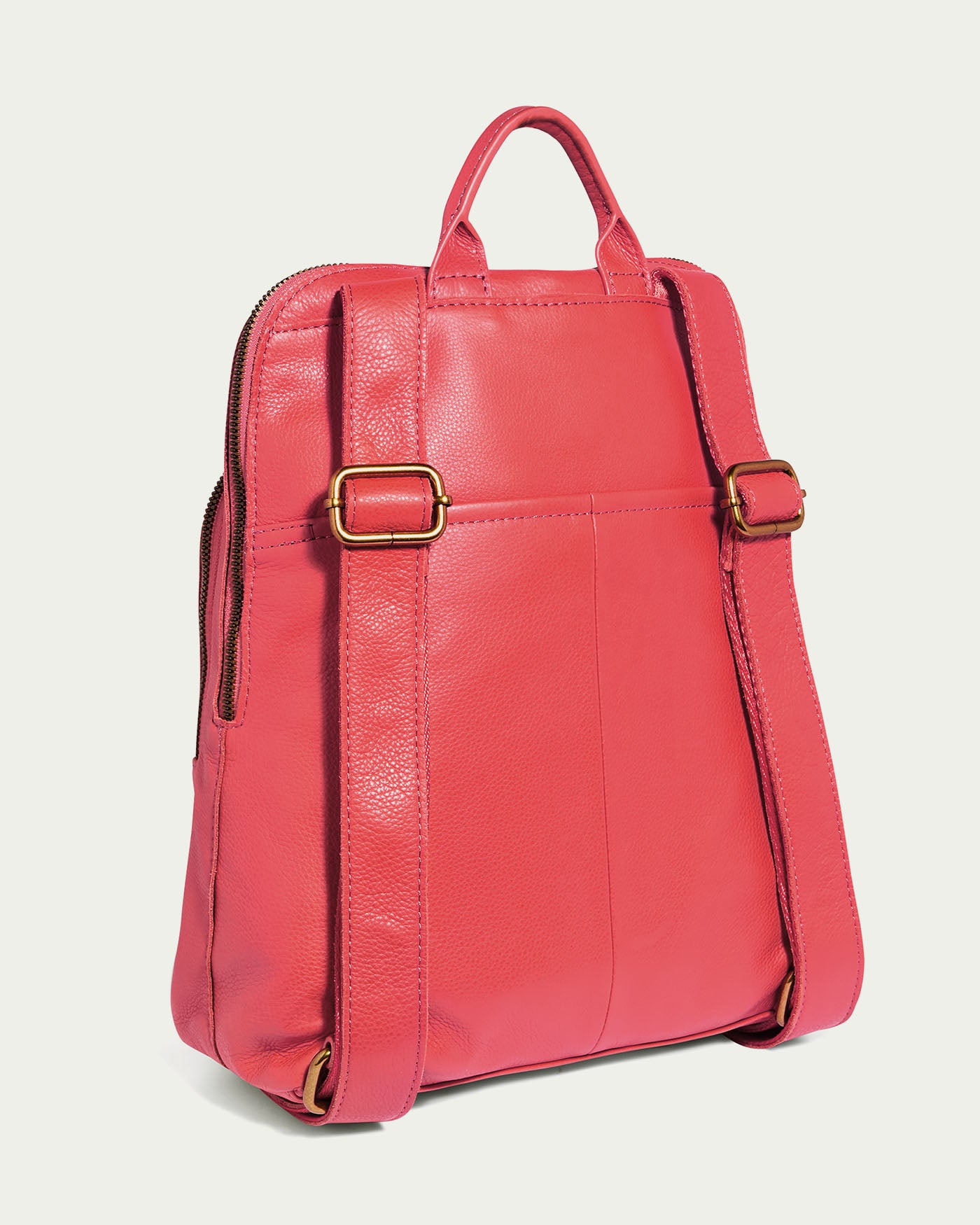 The Cleveland Backpack by American Leather Co. is displayed from the back in vibrant coral pink. It features adjustable leather straps with brass buckles, a top handle, smooth genuine leather texture, and a side zipper.