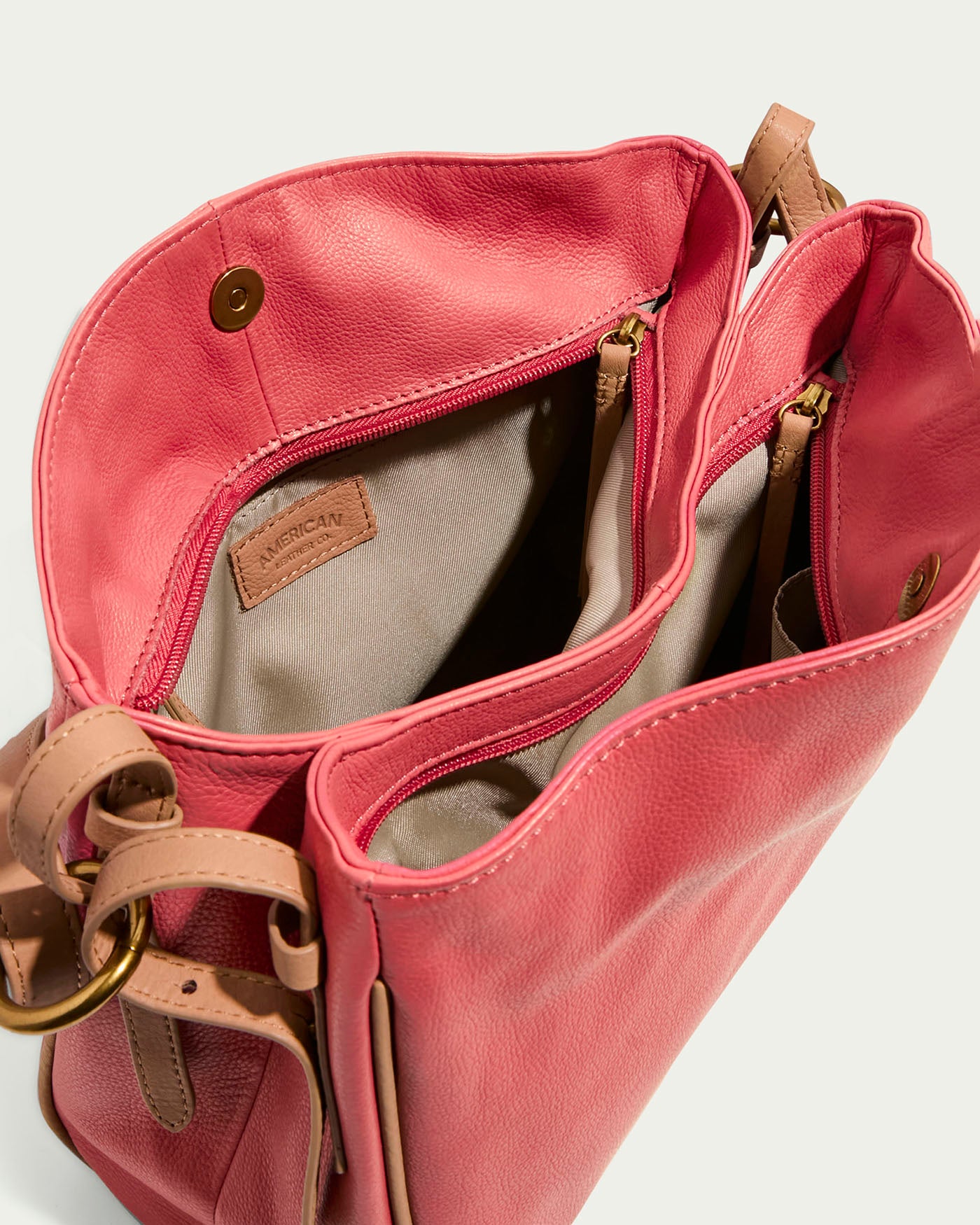 Open pink Dean Double Entry Convertible Hobo by American Leather Co., featuring tan glove leather accents, multiple compartments, magnetic closures, beige lining with a stitched label inside, and an adjustable strap for convenience, set against a light background.