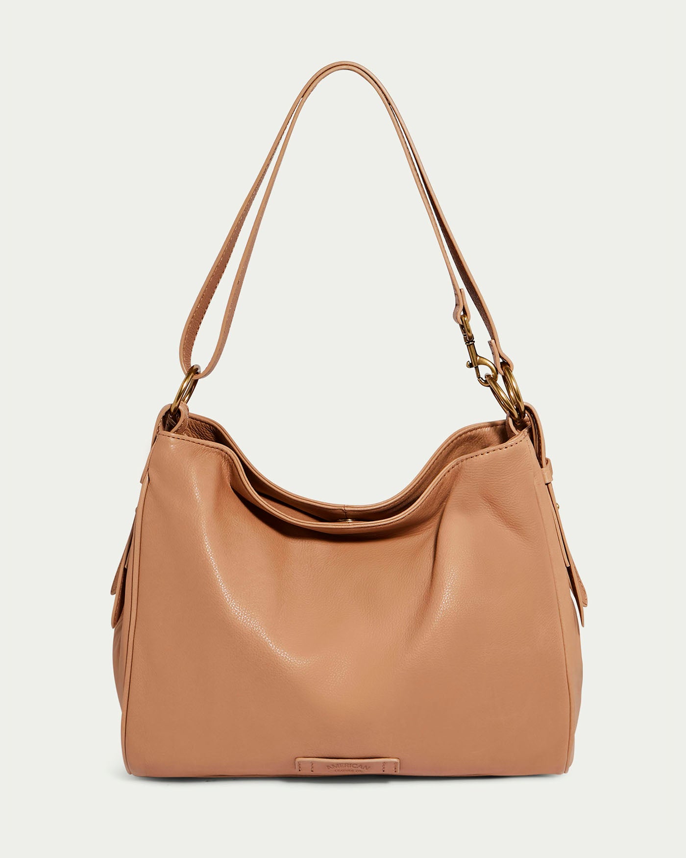 The Dean Double Entry Convertible Hobo by American Leather Co. is a nutmeg leather shoulder bag with a minimalist design, slouchy body, adjustable strap, soft glove leather, subtle gold-toned hardware, and a small logo plate on the front against a plain light gray background.