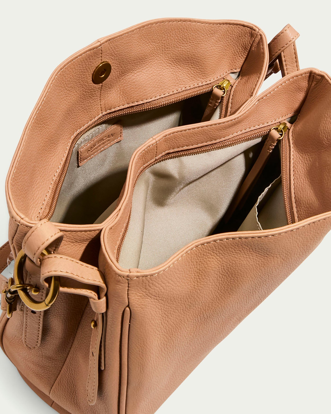 The Dean Double Entry Convertible Hobo by American Leather Co. is a tan glove leather handbag with gold hardware, beige fabric lining, multiple compartments, two handles, and an adjustable strap for versatility. It features an open top with zippers and a decorative buckle.