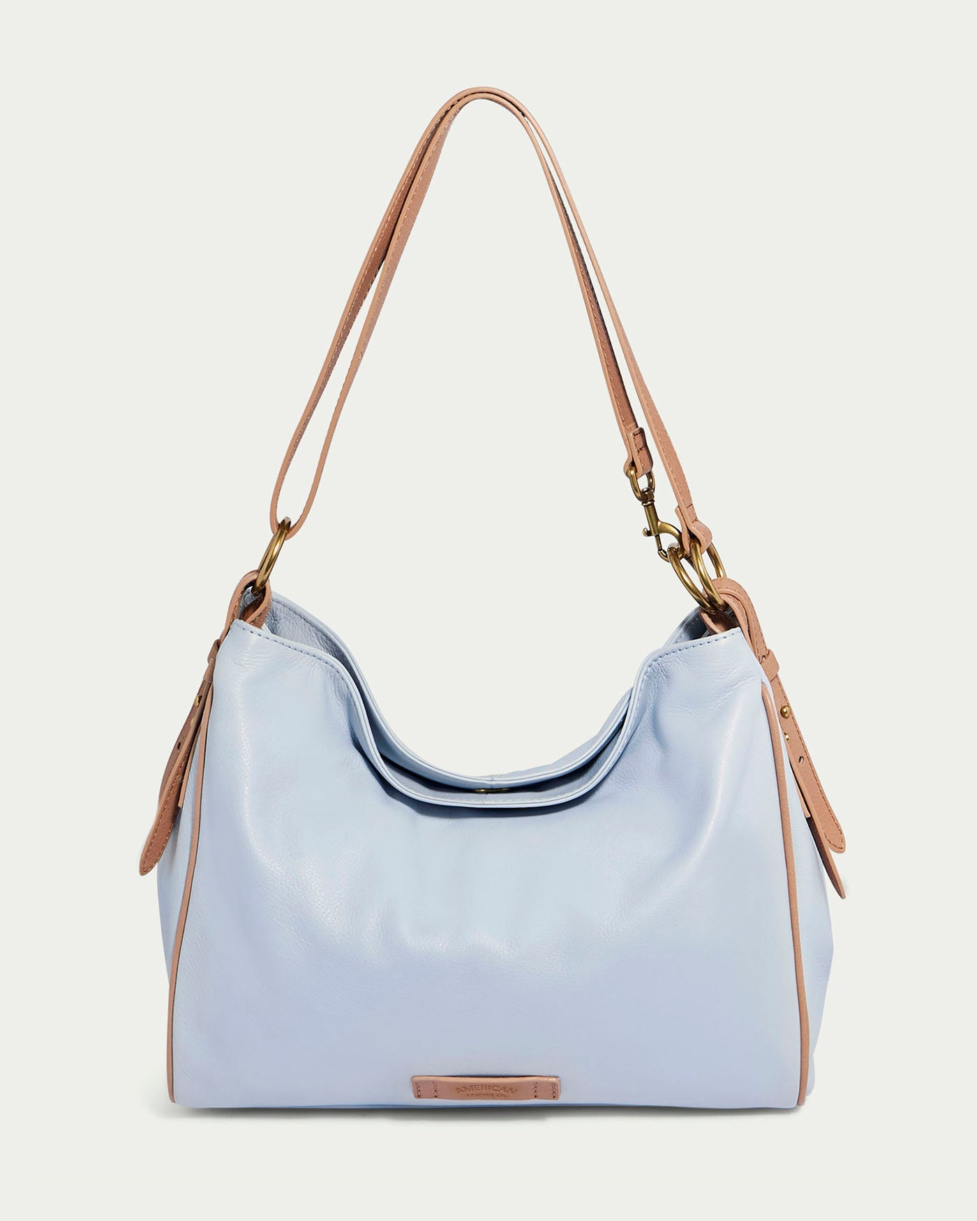 The American Leather Co. Dean Double Entry Convertible Hobo, in Oasis Blue with Nutmeg straps, showcases elegant gold hardware. Its soft shape includes a small rectangular logo tag and adjustable straps with rivets for versatile wear.