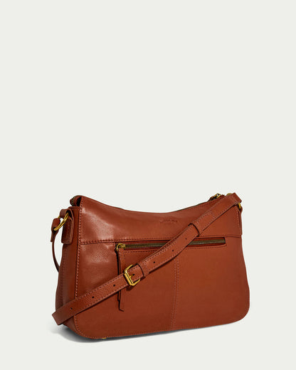 The American Leather Co. Holton Crossbody is a spacious bag made from brown glove leather, with a front zip pocket and adjustable strap. Gold-tone hardware and a smooth finish stand out against a light background, offering both style and functionality.