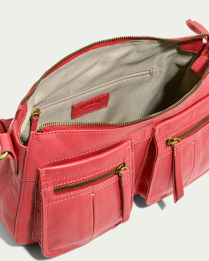 The American Leather Co. Holton Crossbody in coral glove leather features a partially open zipper over a beige interior, with two front pockets adorned with gold zippers and tab pulls. It includes an adjustable strap, all set against a light, neutral backdrop.