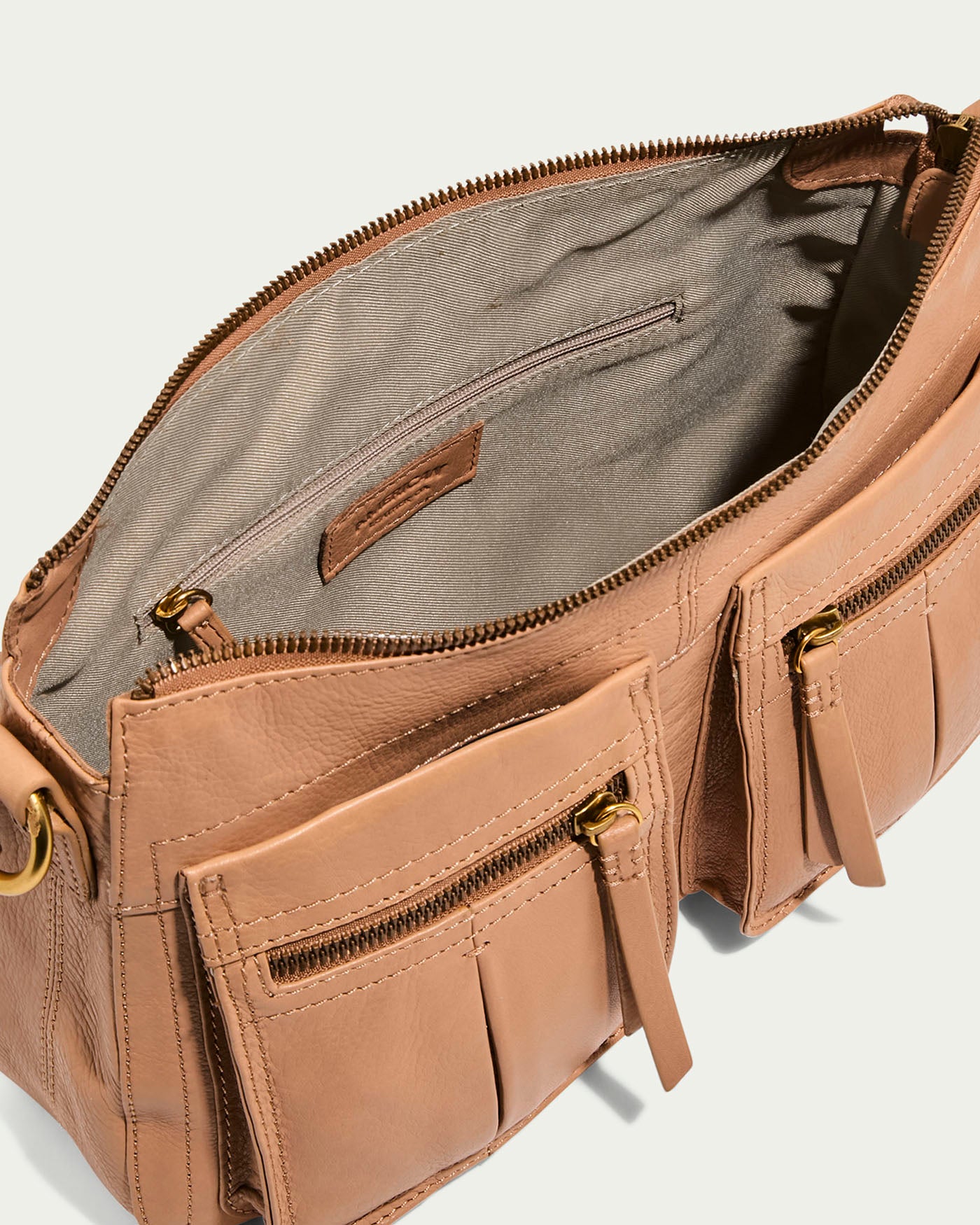 The Holton Crossbody by American Leather Co. is a tan glove leather handbag with two exterior pockets featuring zipper and tassel details, an open crossbody design with a spacious interior, a zippered pocket, and gold-tone hardware for elegance.