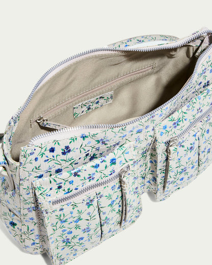 The American Leather Co. Holton Crossbody is a white floral glove leather backpack with blue and green flowers. It features multiple front zip pockets, an open main compartment with a zipper, and a small internal pocket—all lined in beige fabric.