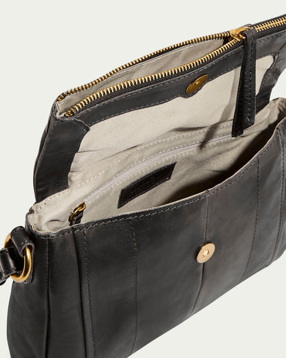 The Lee Double Entry Crossbody by American Leather Co. is a black genuine leather handbag with an open top revealing a beige interior. It includes a zippered pocket, button closure main compartment, gold hardware, adjustable strap, and circular attachment for versatile wear.