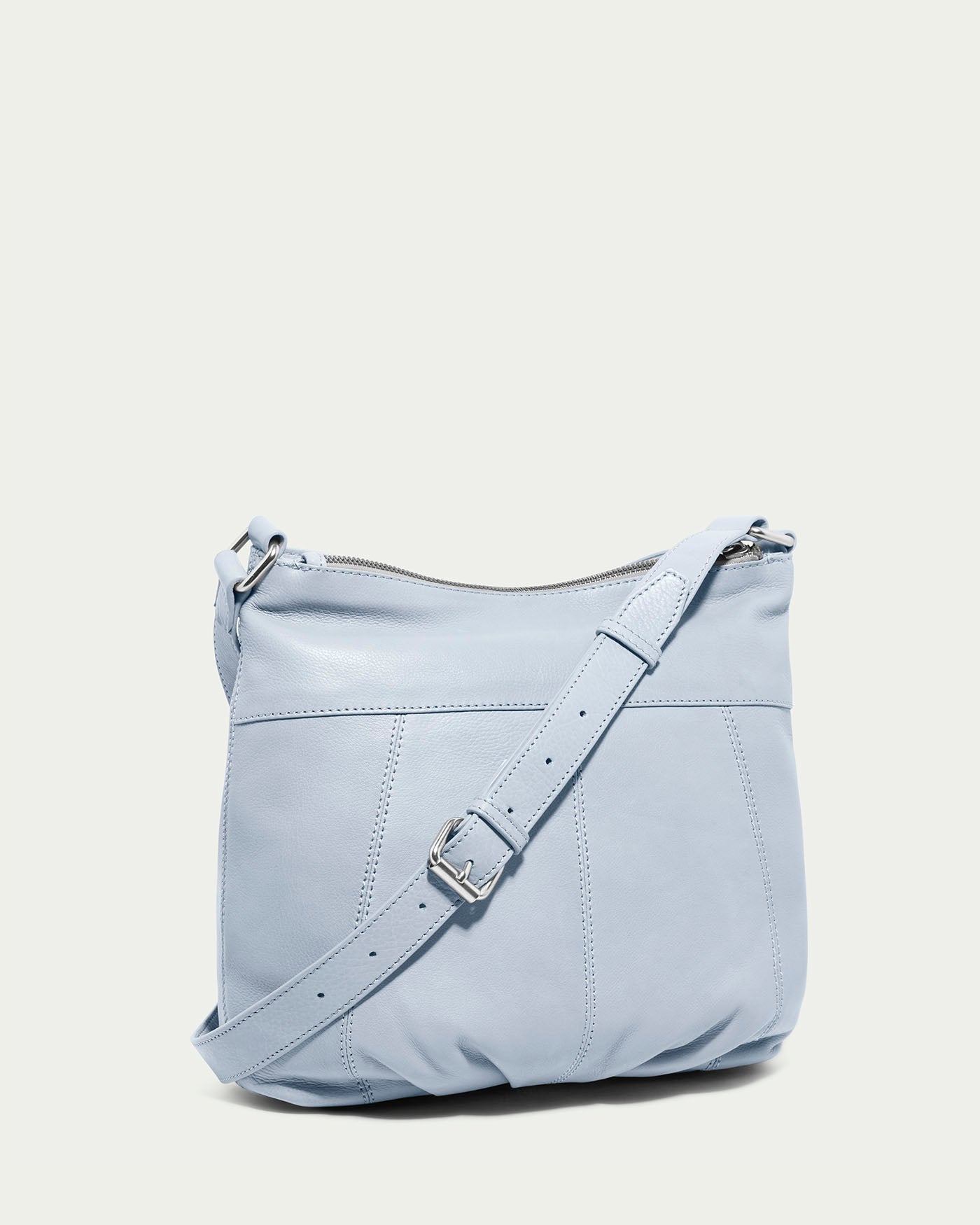 The Lennie Double Entry Crossbody by American Leather Co. is a light blue leather handbag featuring an adjustable strap with a silver buckle and subtle stitching lines, set against a plain off-white background.