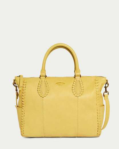 The Madison Satchel by American Leather Co. is a Biscotti-colored handbag crafted from glove leather. It features short handles, a detachable shoulder strap, decorative stitching, hand-woven edge detailing, an embossed center logo, and boasts a structured shape with a soft, smooth texture.