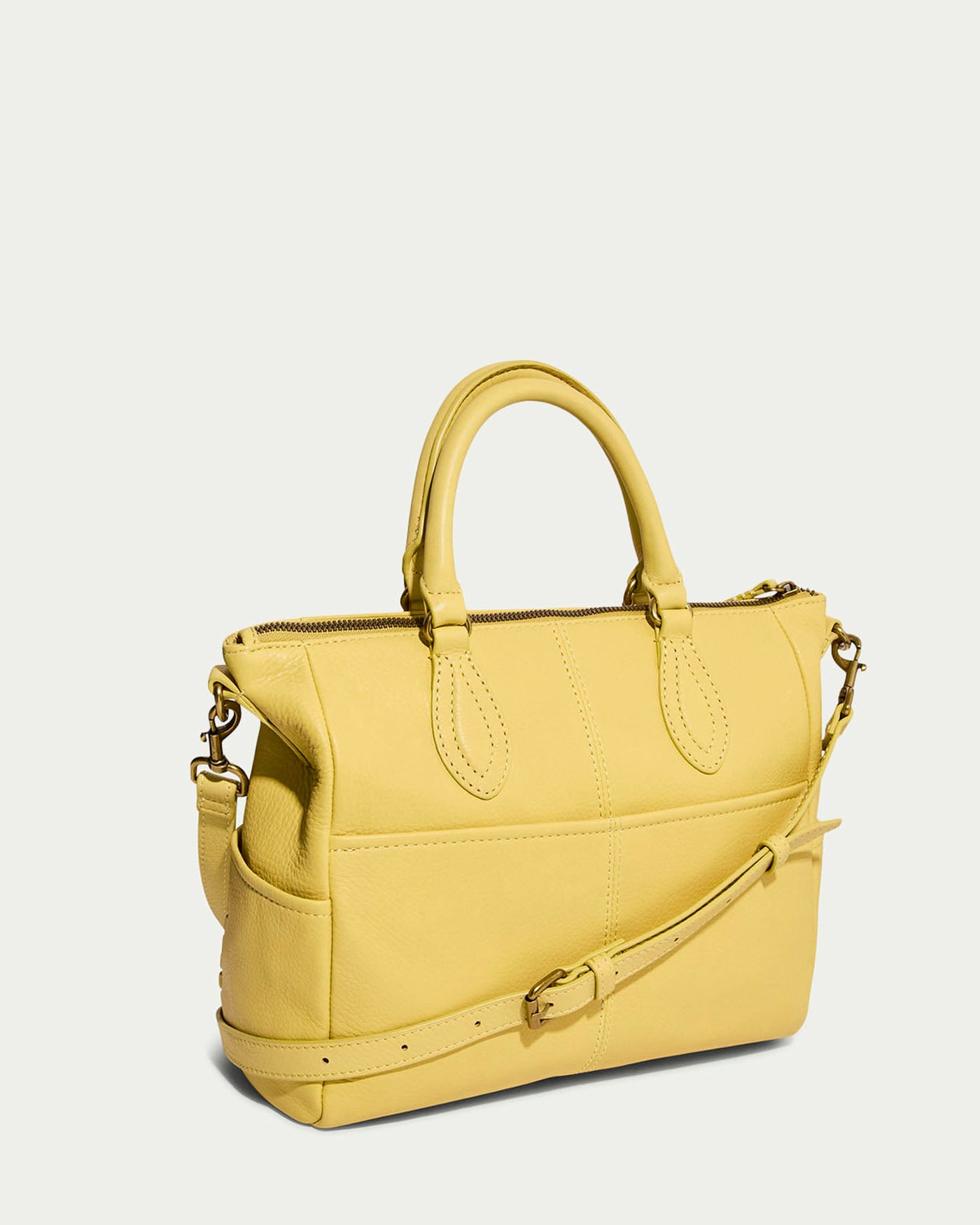 The Madison Satchel by American Leather Co. is a yellow glove leather bag featuring two short handles and a detachable shoulder strap, with a zip closure on top, offering a simple yet elegant design suitable for any occasion.