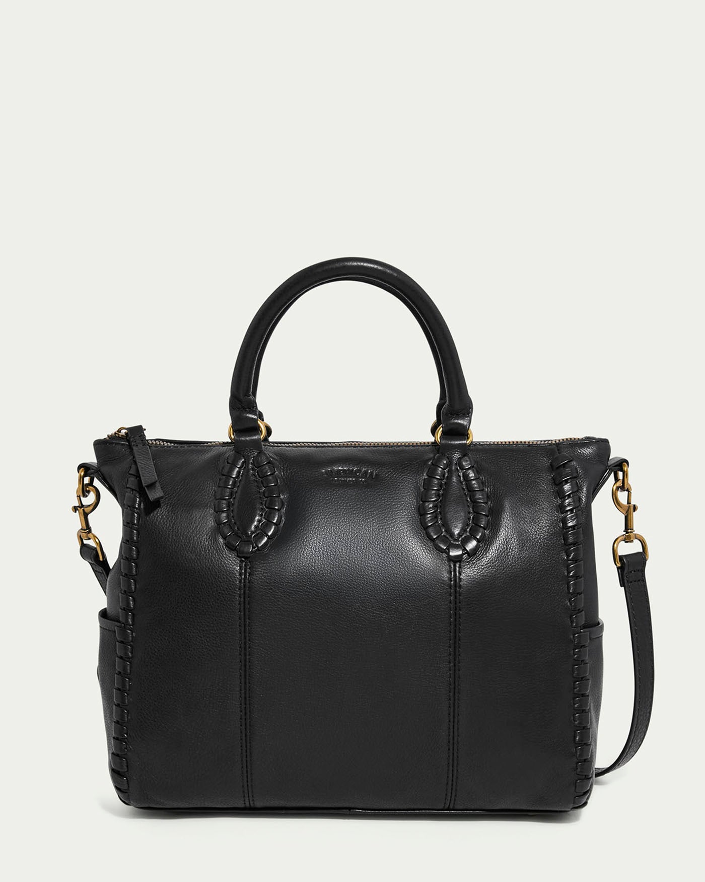 The Madison Satchel by American Leather Co. is a black glove leather handbag with dual handles, detachable shoulder strap, and gold hardware. It features decorative stitching, hand-woven detailing, a visible top zipper, and the brand name embossed near the top center.