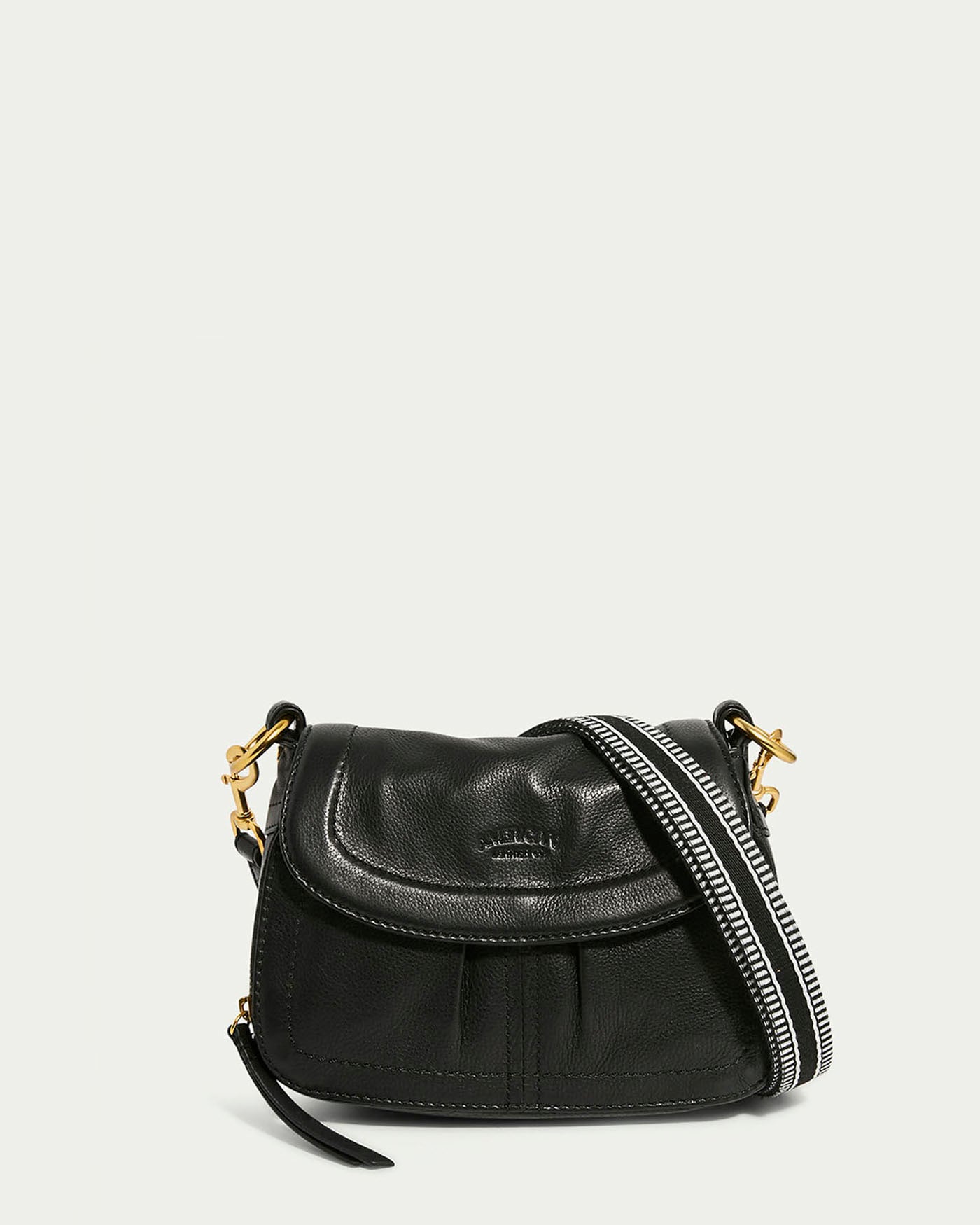 The Marino Mini Crossbody by American Leather Co. is displayed against a plain background. Made from black glove leather, it features a curved flap, gold clasps, and an adjustable black-and-white striped shoulder strap draped across the front.