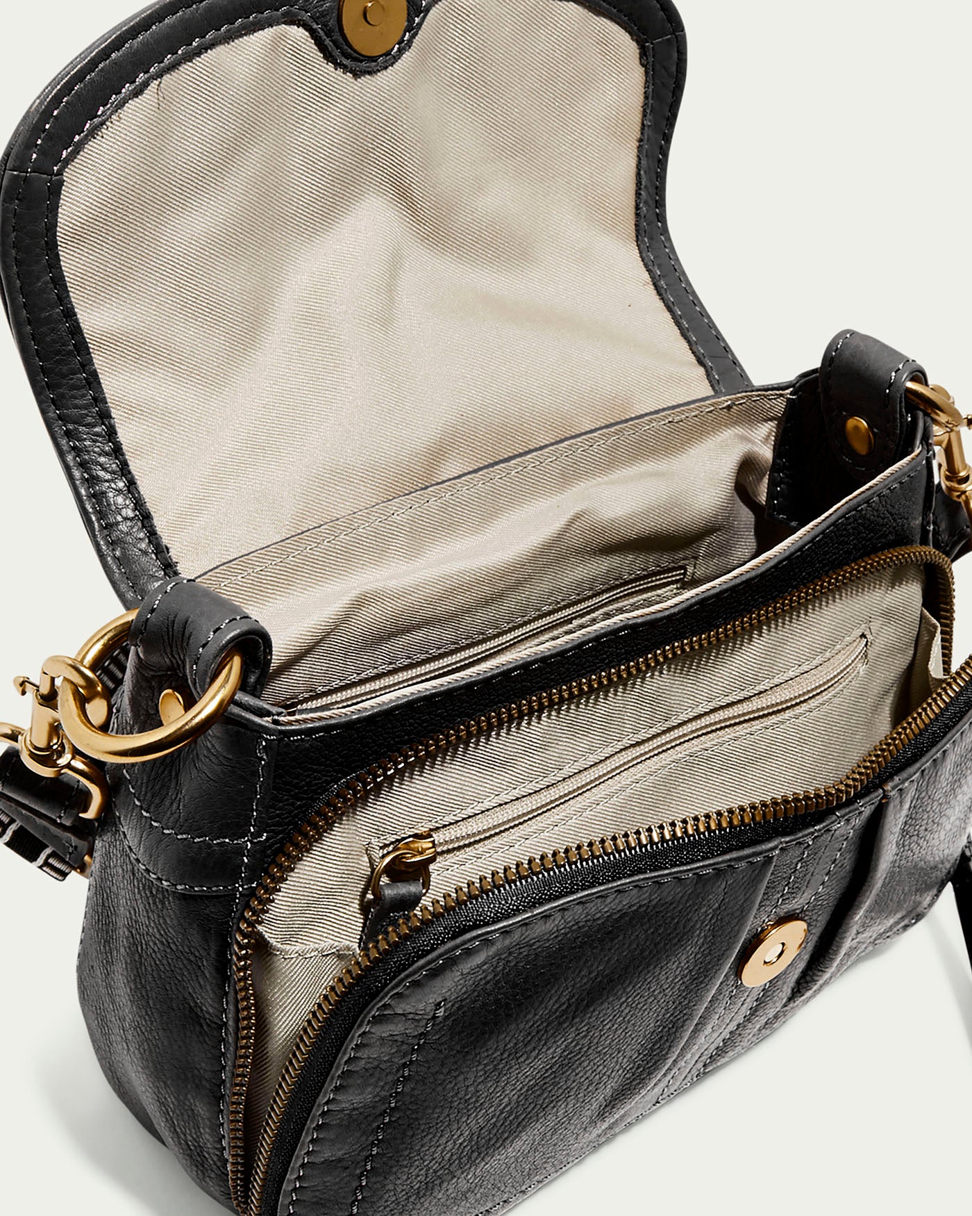 The Marino Mini Crossbody by American Leather Co. is an open black glove leather handbag with a magnetic snap closure and gold hardware. It features a beige interior with multiple compartments, a zippered front pocket, and detachable, adjustable straps secured by gold rings.