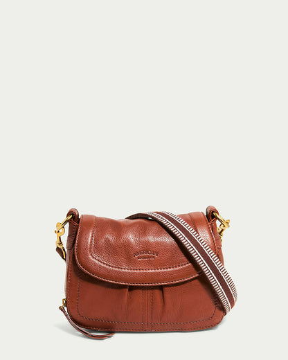 The Marino Mini Crossbody from American Leather Co. is crafted from rich brandy glove leather with an adjustable striped shoulder strap and brass hardware. The embossed brand name graces the flap, and its curved design with intricate stitching stands out against a plain white background.