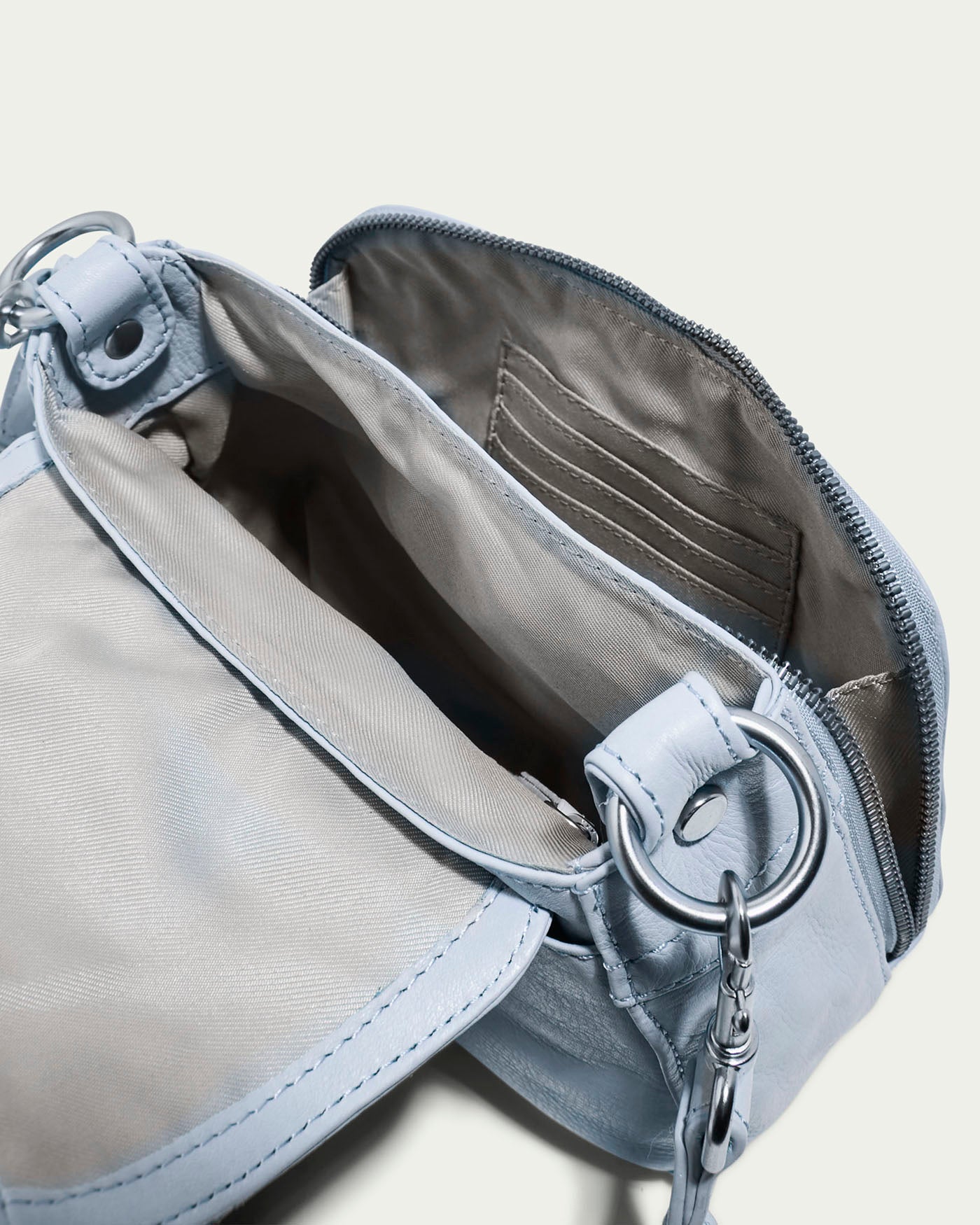 The Marino Mini Crossbody by American Leather Co. in light blue unveils a beige lining with inner compartments via its top unzip. Featuring a metallic chain strap connected by rings, it's perfectly complemented by luxurious glove leather.