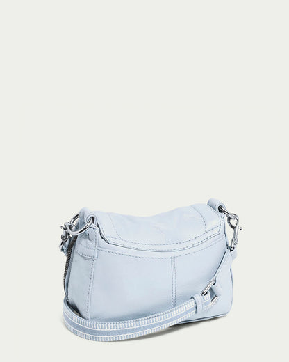 The Marino Mini Crossbody by American Leather Co. is a light blue shoulder bag with textured glove leather, silver-tone hardware, and stitching details. It features a zippered main compartment and an adjustable strap, set against an off-white background in a soft, curved design.