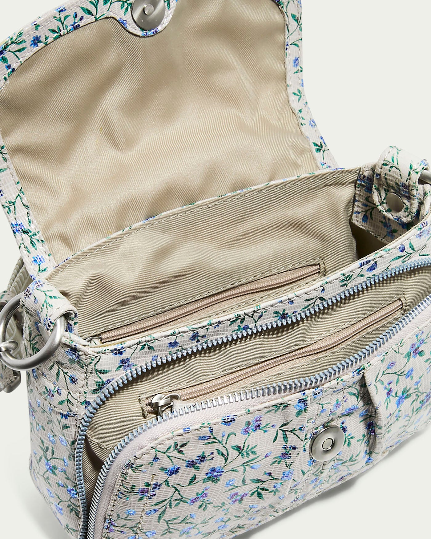 The Marino Mini Crossbody by American Leather Co. features a floral pattern with an open top, beige lining, glove leather accents, front zip pocket, interior compartment, and button clasp on the flap. It's equipped with an adjustable strap and silver rings for versatile wear.