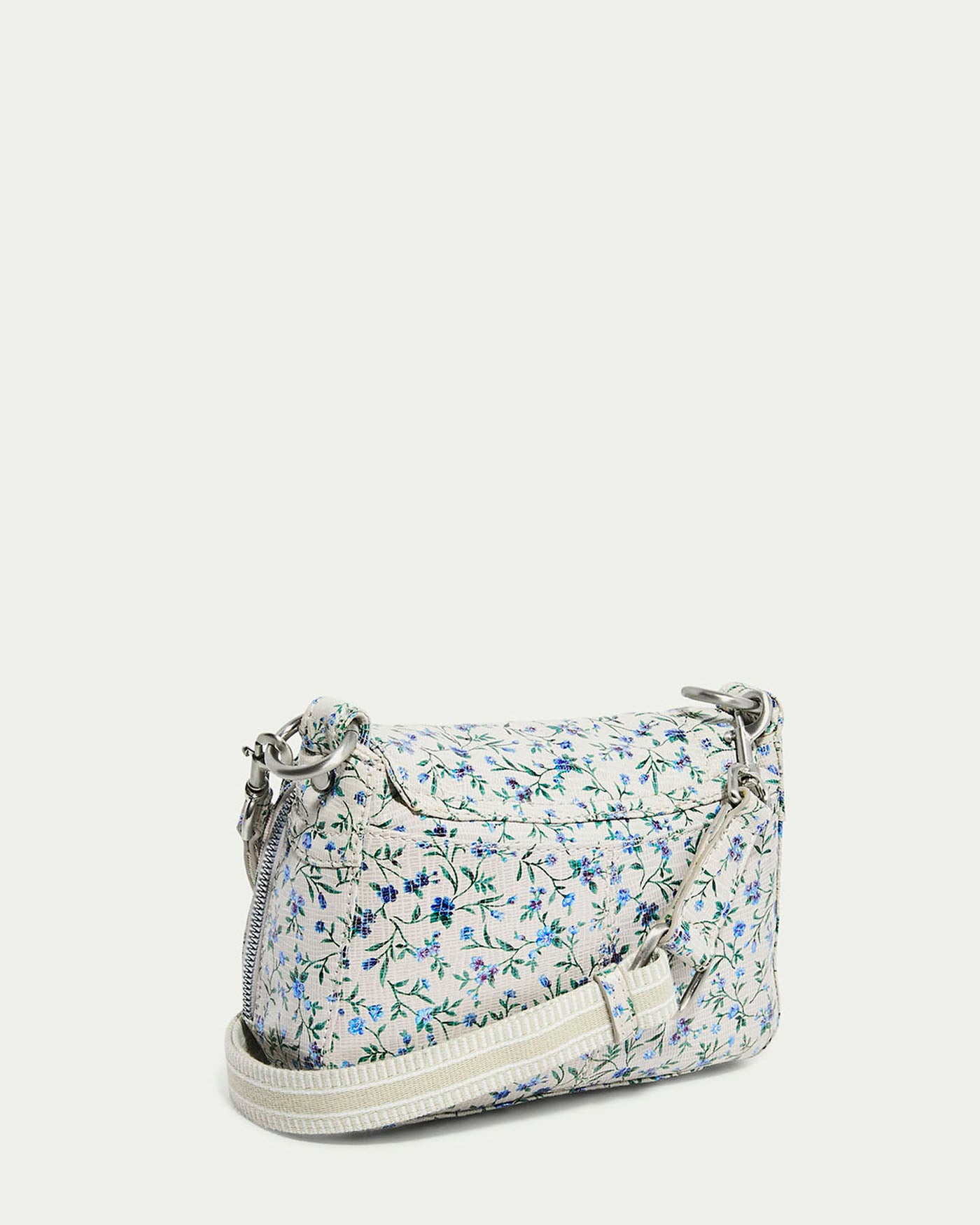 The Marino Mini Crossbody by American Leather Co. features a floral pattern in blue and green on white, with a glove leather exterior, long adjustable strap, and silver hardware. Its compact rectangular design combines style and function against a light neutral backdrop.