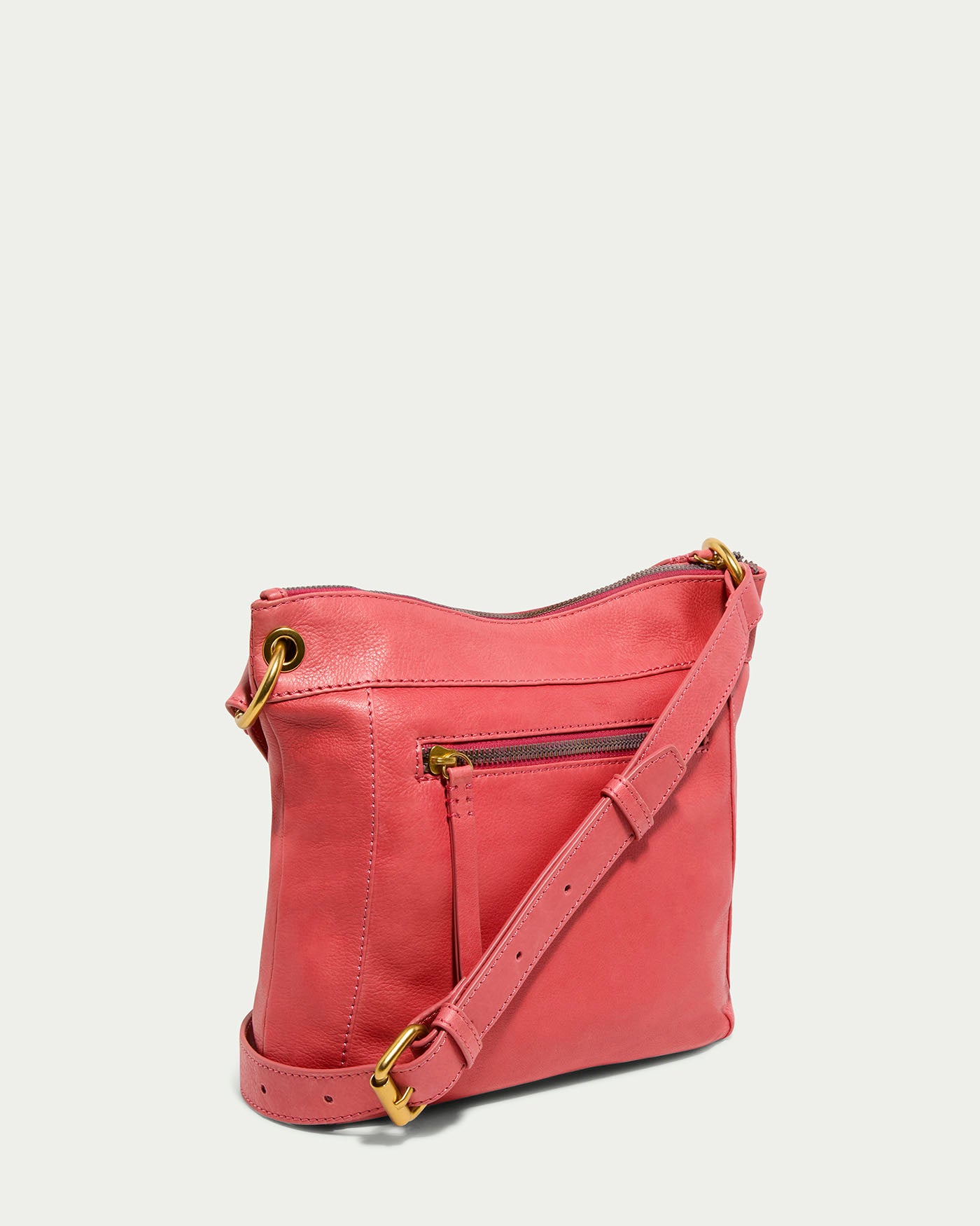 The Sherryl Crossbody from American Leather Co. is a pink crossbody bag made from glove leather with gold hardware. It includes a zippered main compartment, front zip pocket, and adjustable strap, displayed at an angle to show its side and front.