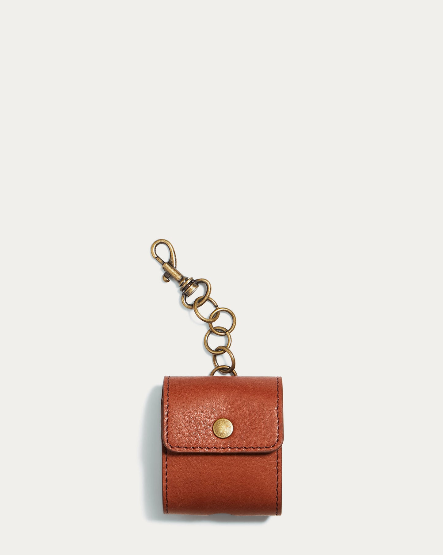 The Flagstaff Airpod Case by American Leather Co. is a compact pouch made from authentic American leather, designed with a brass snap button and clip chain ideal for use as an AirPods bag charm. It features an opening for a charger cord, making it perfect for holding small accessories, and is presented against a plain white background.