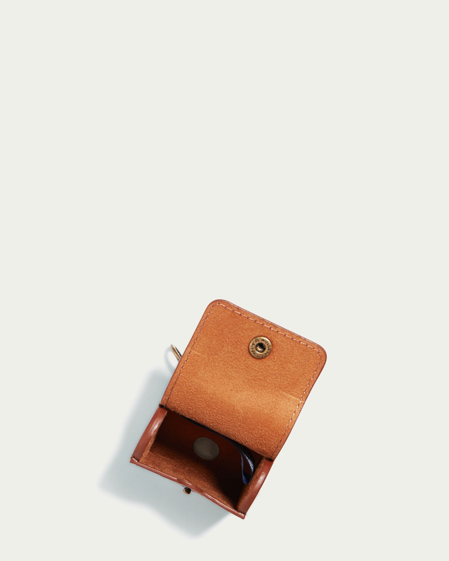 The Flagstaff Airpod Case by American Leather Co., crafted from genuine brown leather, is showcased against a plain white background. The open case reveals its interior, featuring a snap closure on the flap and an elegantly designed opening for easy charger cord access, combining practicality with style.