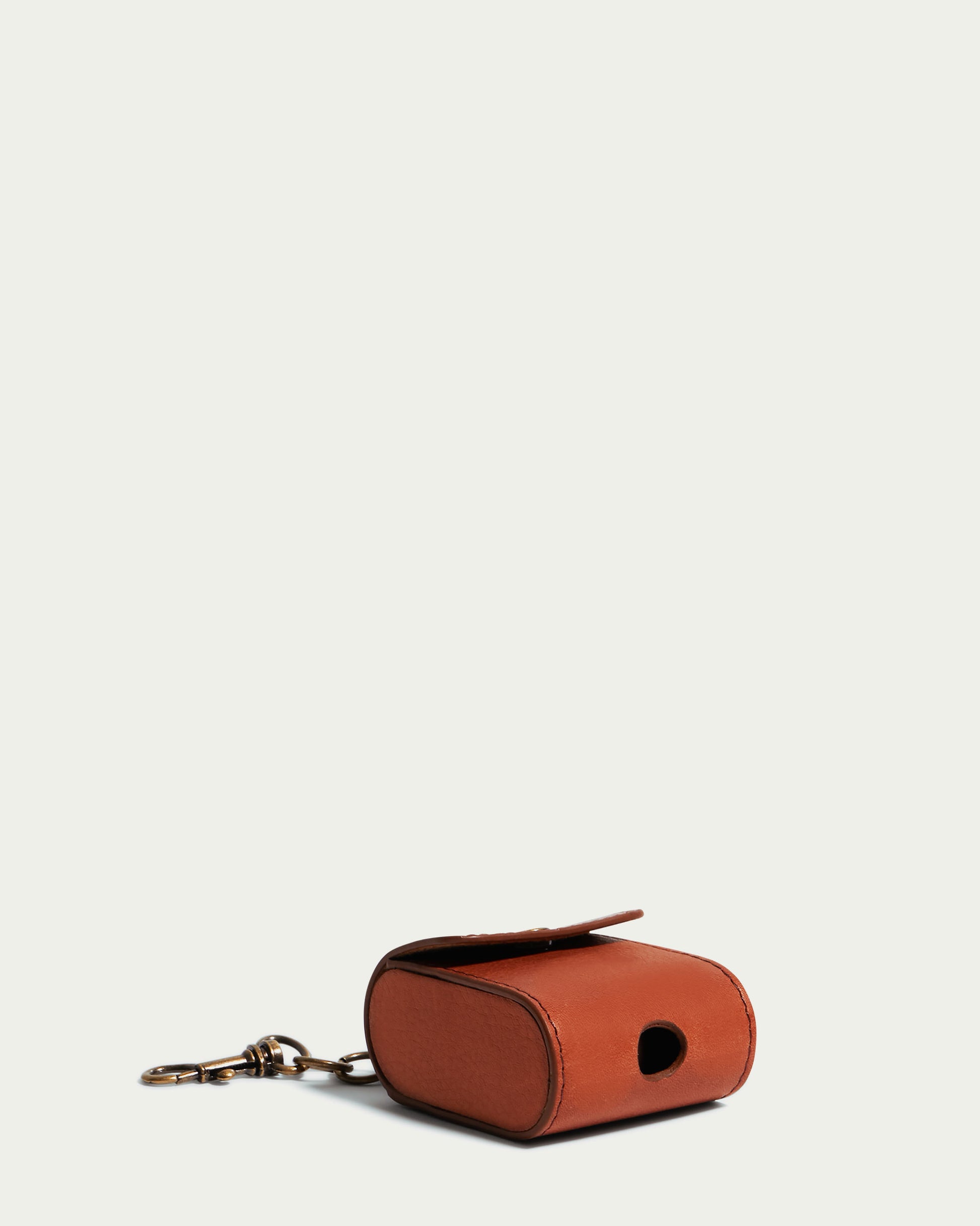 The Flagstaff Airpod Case, made by American Leather Co., is a compact and stylish brown leather keychain pouch constructed from authentic American leather. It features a circular opening on one side, making it ideal as an AirPods bag charm. The pouch is attached to a sturdy metal keyring, set against a plain off-white background.