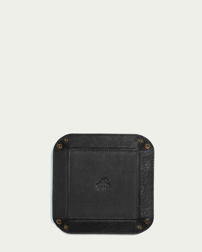 A square black leather tray with rounded corners and antiqued brass rivets at each corner, embossed with a decorative design in the center, the Manchester Leather Tray by American Leather Co. is set against a plain light background to showcase genuine leather craftsmanship.