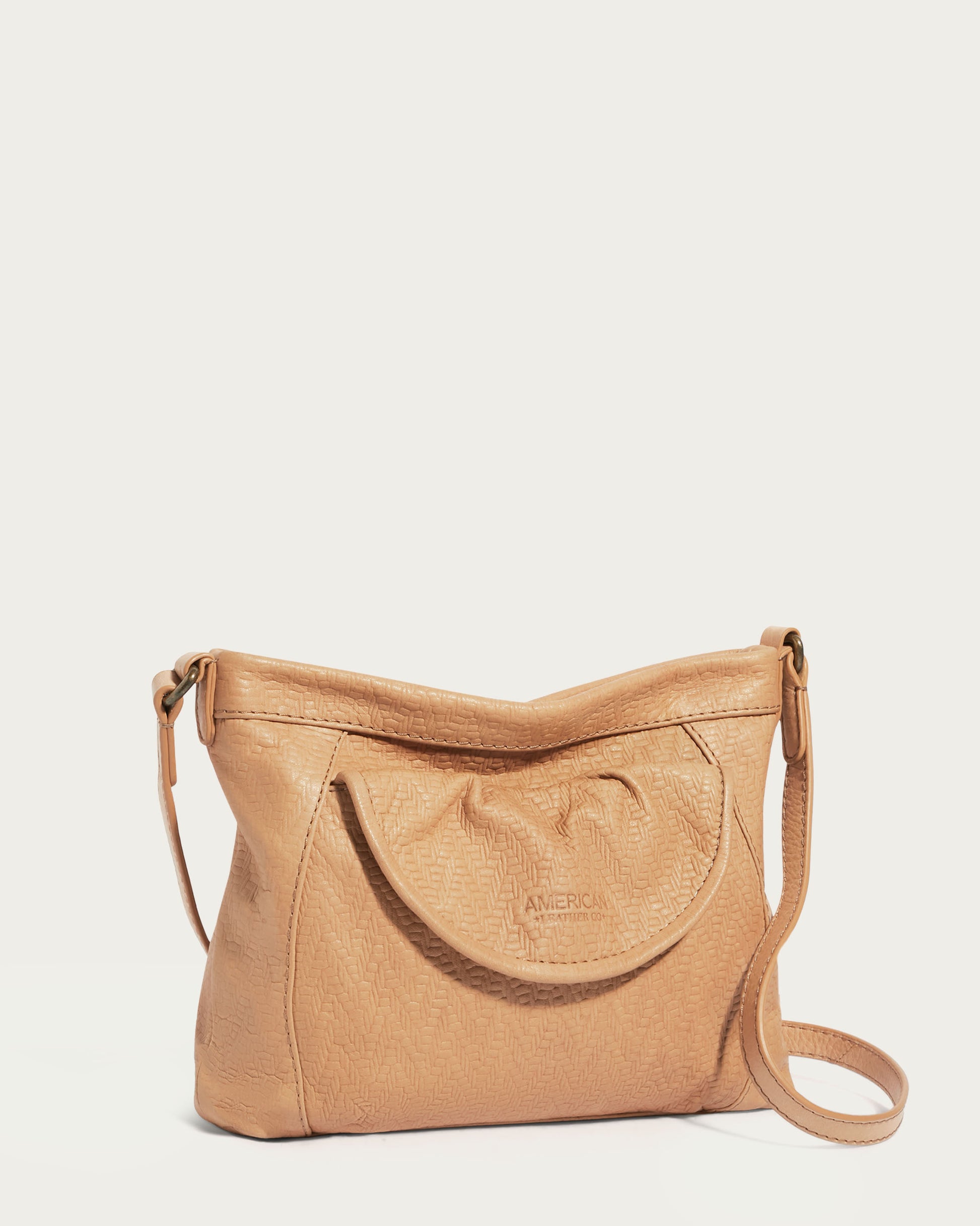 The Reed Crossbody by American Leather Co. is made from glove leather and showcases a tan hue with an embossed texture on the flap pocket. The discreet 'AMERICAN LEATHER CO.' logo provides an elegant detail, and the adjustable crossbody strap allows for versatile use and stylish simplicity.