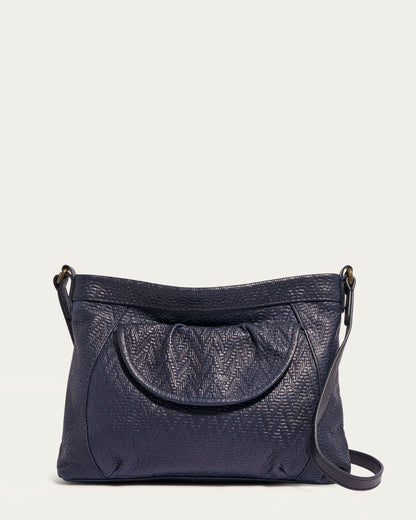 The Reed Crossbody by American Leather Co. is an elegant handbag made from luxurious glove leather, characterized by its textured finish. It features a rounded top with subtle pleating and includes a long crossbody strap for effortless carrying. Set against a plain, light background, this bag perfectly merges style with functionality.