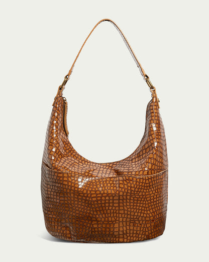 The Carrie Hobo from American Leather Co. is a stylish bag crafted from brown genuine American leather with a crocodile pattern, complete with a shoulder strap. It features a shiny finish and spacious classic design, presented against a plain background.