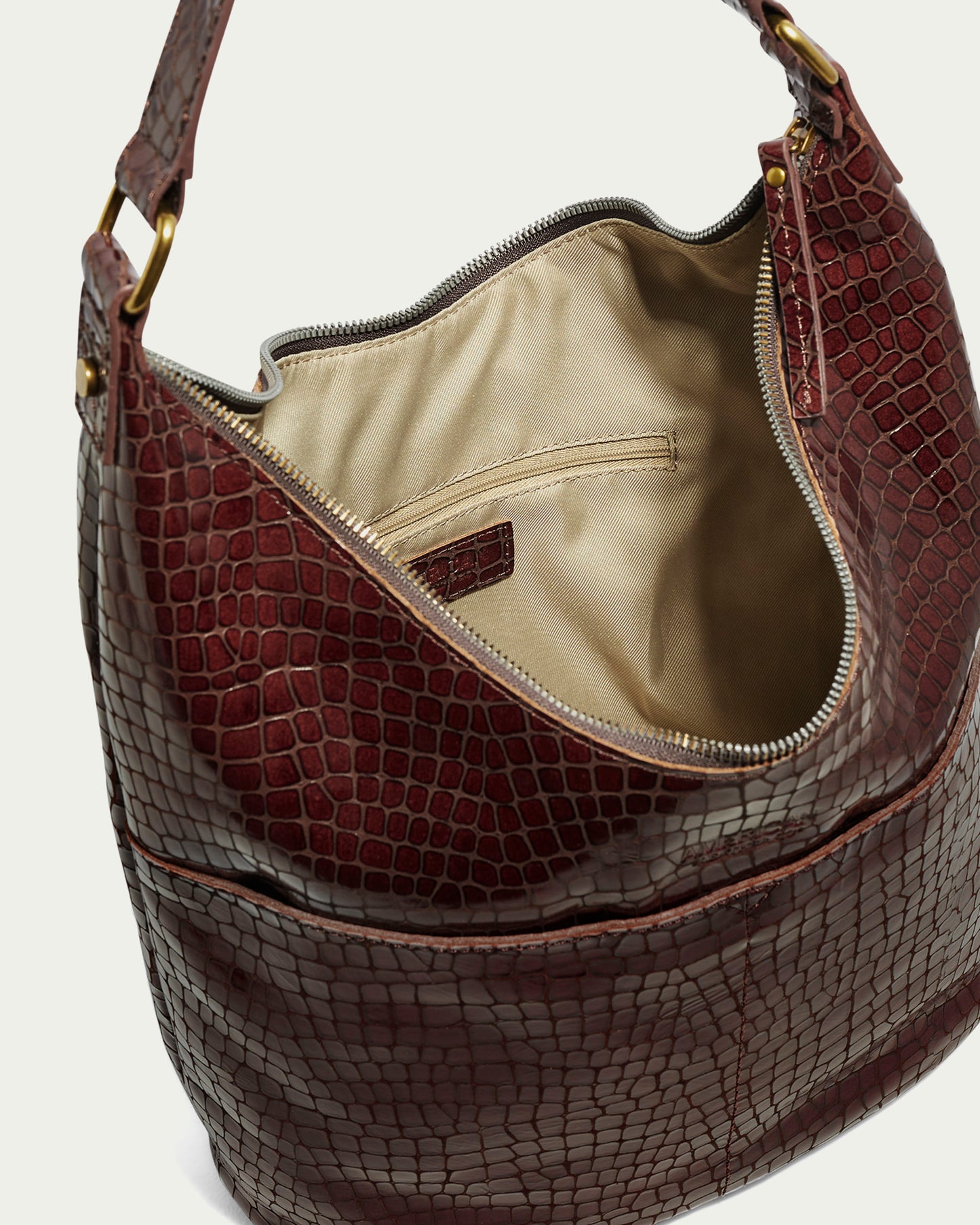 The Carrie Hobo by American Leather Co. is a sophisticated brown leather handbag with a crocodile pattern, made from authentic American leather. It features an open top that displays a beige interior lining and includes a small inner pocket. Adorned with gold hardware and equipped with a short strap, this classic piece embodies timeless elegance.