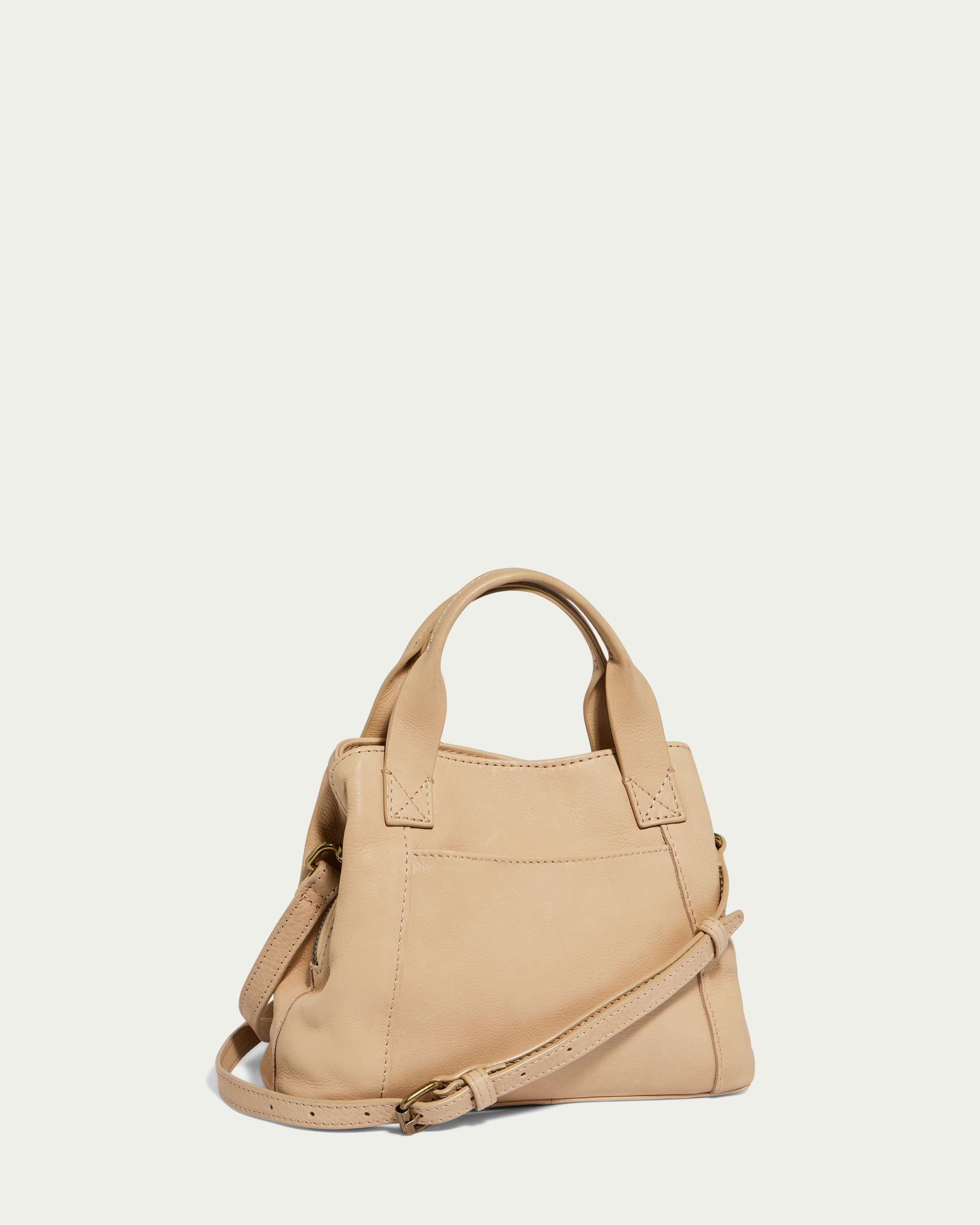 The Ada Triple Entry Crossbody by American Leather Co. is a small, beige handbag with a minimalist design featuring short handles and a long adjustable shoulder strap. Crafted from genuine leather, this satchel boasts a simple and elegant appearance, making it suitable for both casual and formal use. It is set against a plain off-white background.