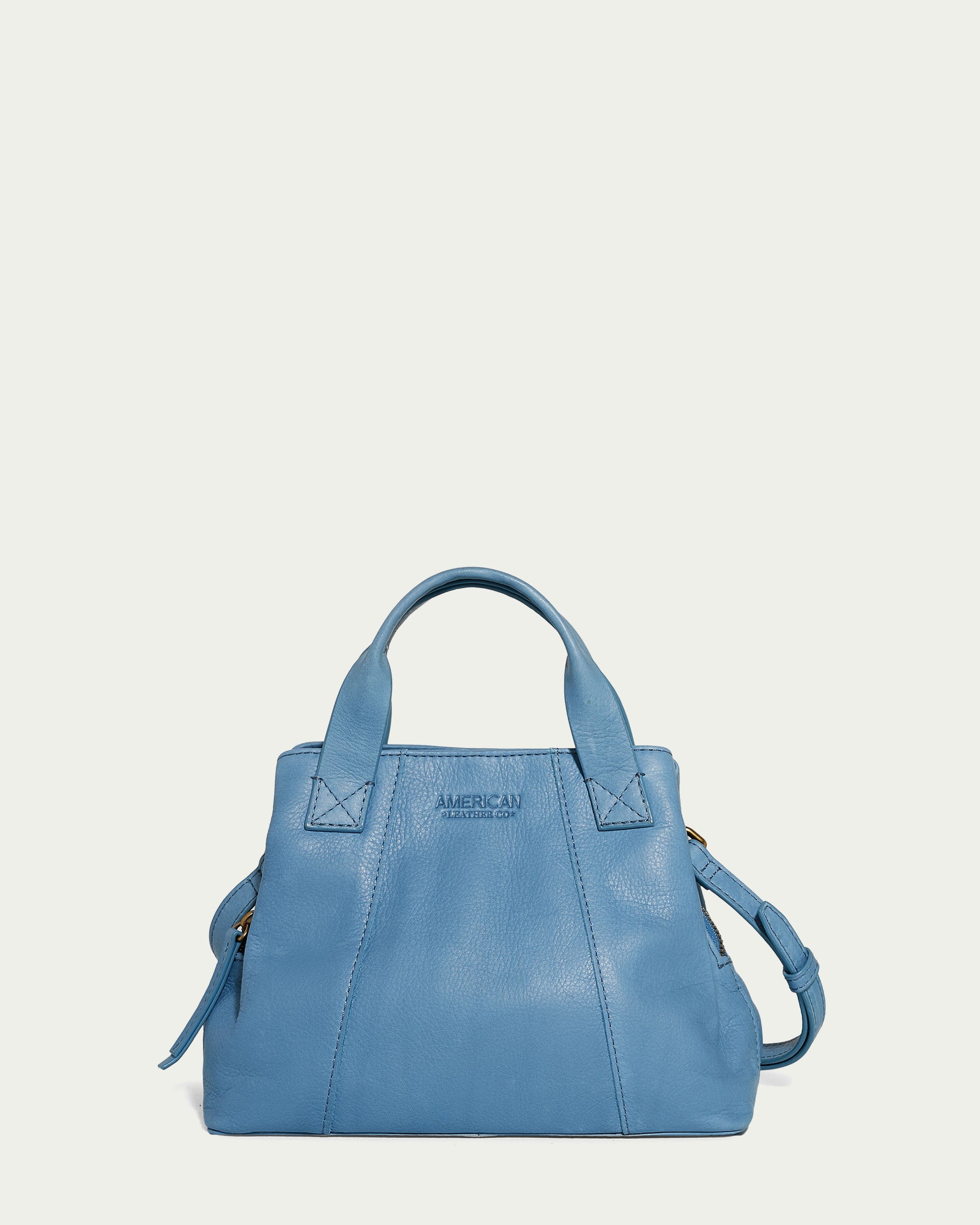 The Ada Triple Entry Crossbody, a light blue genuine leather handbag from American Leather Co., is showcased against a plain background. It boasts two sturdy top handles and includes a detachable crossbody strap. The front is elegantly embossed with "American Leather Co." and its triple entry design gives it a chic, structured square shape.