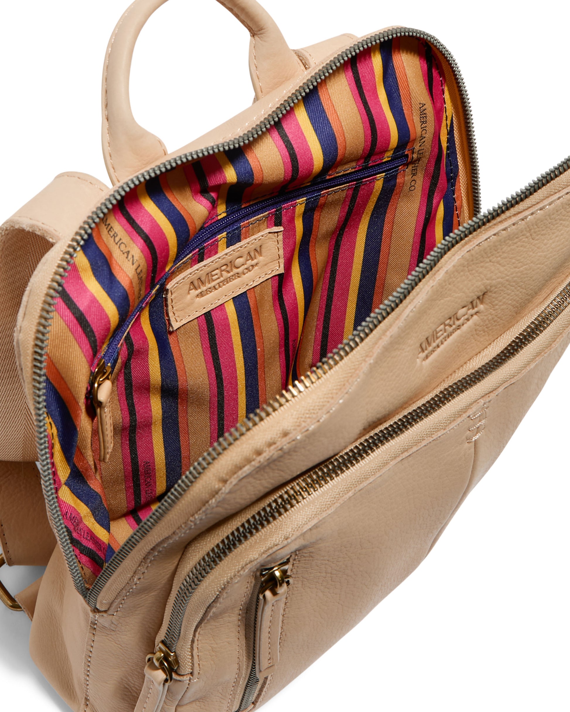 The Cleveland Midsize Backpack by American Leather Co. features a beige leather exterior with an open top that reveals a colorful striped interior in red, orange, purple, and brown hues. It includes zip compartments on the interior and exterior and has a stitched "AMERICAN" label inside.