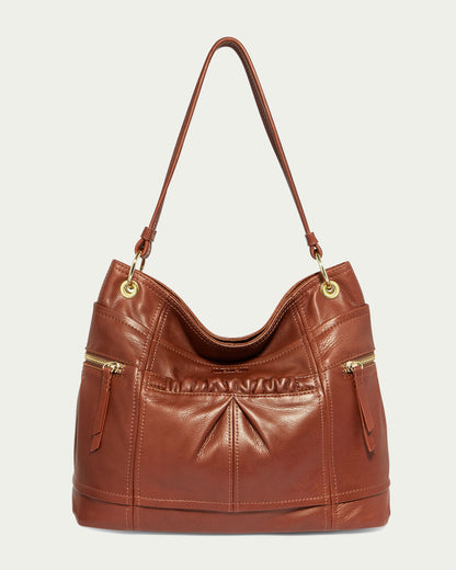 The Tenafly Hobo by American Leather Co. is a brown genuine leather shoulder bag designed with two front zipper pockets and a single strap. This stylish and functional Hobo bag features gold-tone hardware and boasts a slightly slouched design.
