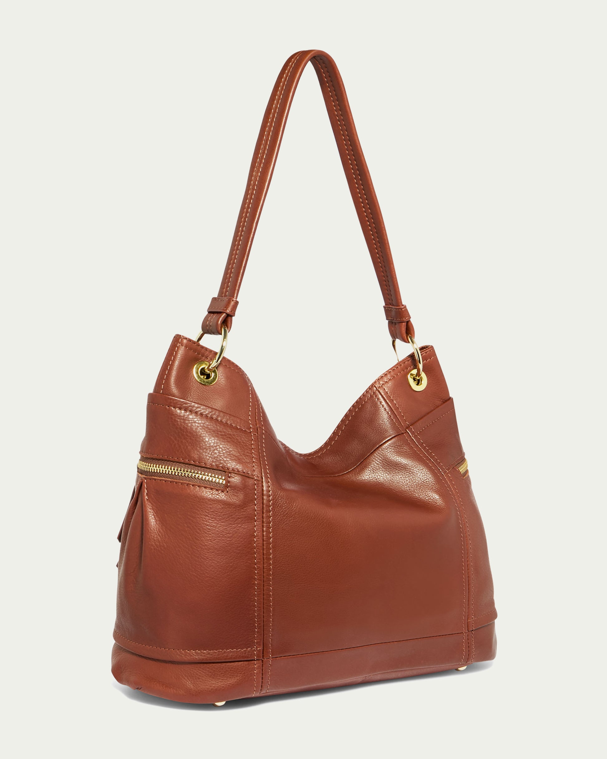 The Tenafly Hobo by American Leather Co. is a brown hobo handbag made from genuine leather, featuring two handles and gold-toned hardware. It includes multiple side zipper pockets and a sturdy base, set against a plain, light-colored background.