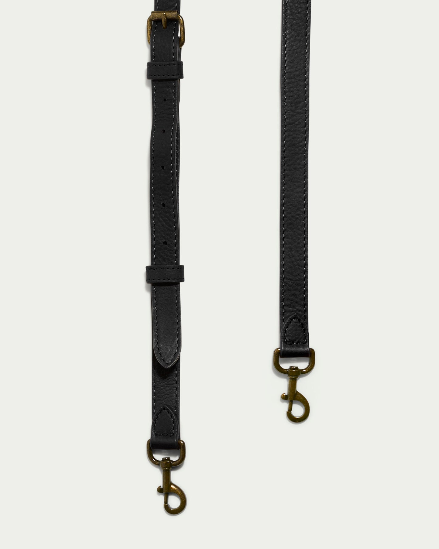 Close-up of two Tall Crossbody Straps in black leather by American Leather Co., showcasing brass clasps against a light background. These genuine leather straps feature adjustable buckles and stitched detailing, making them ideal for a sophisticated crossbody bag.