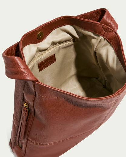 The Virginia Hobo by American Leather Co., made of genuine American leather, is open to showcase its beige fabric interior. It includes artisanal contrast stitching, a front zip pocket, and a magnetic closure, with a structured design featuring two carrying handles.